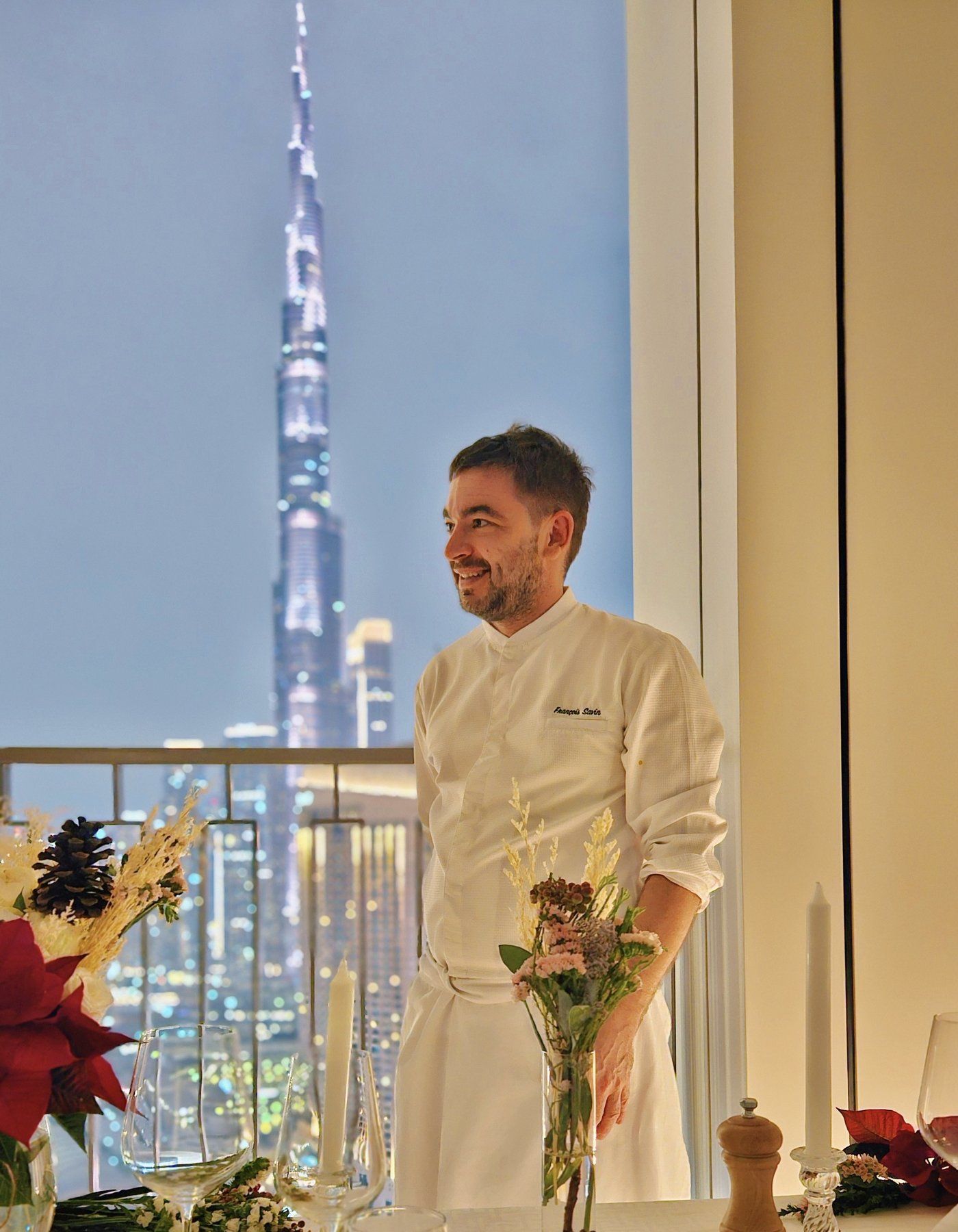 Chef François Savin plating a course on a Dubai terrace, skyline visible in the soft distance.