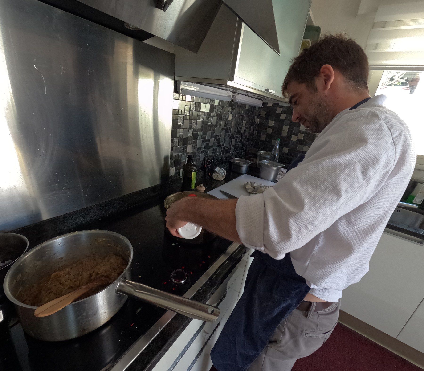 Chef François Savin in his whites, cooking at the stove, a copper pan in hand.