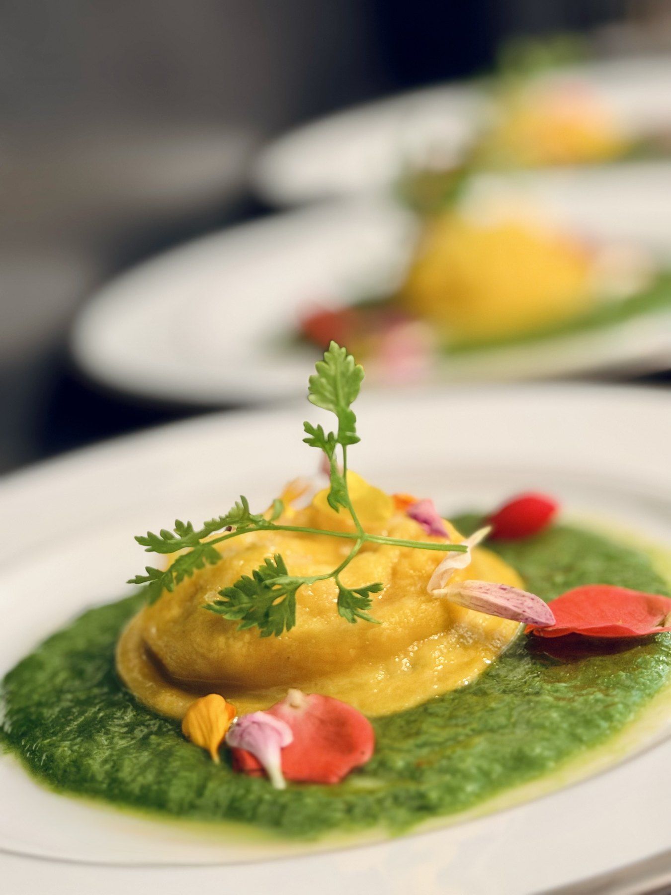A raviolo on a bright green herb sauce, topped with a chervil sprig and flower petals.