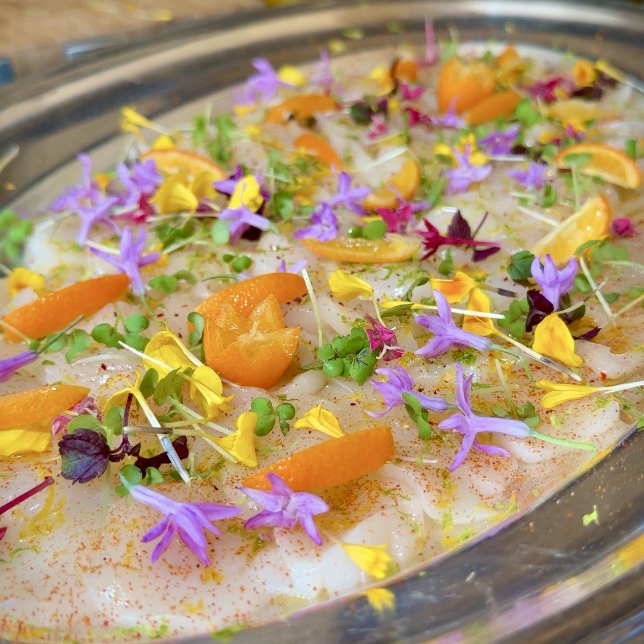 Thinly sliced carpaccio topped with citrus segments, micro herbs and purple and yellow edible flowers.