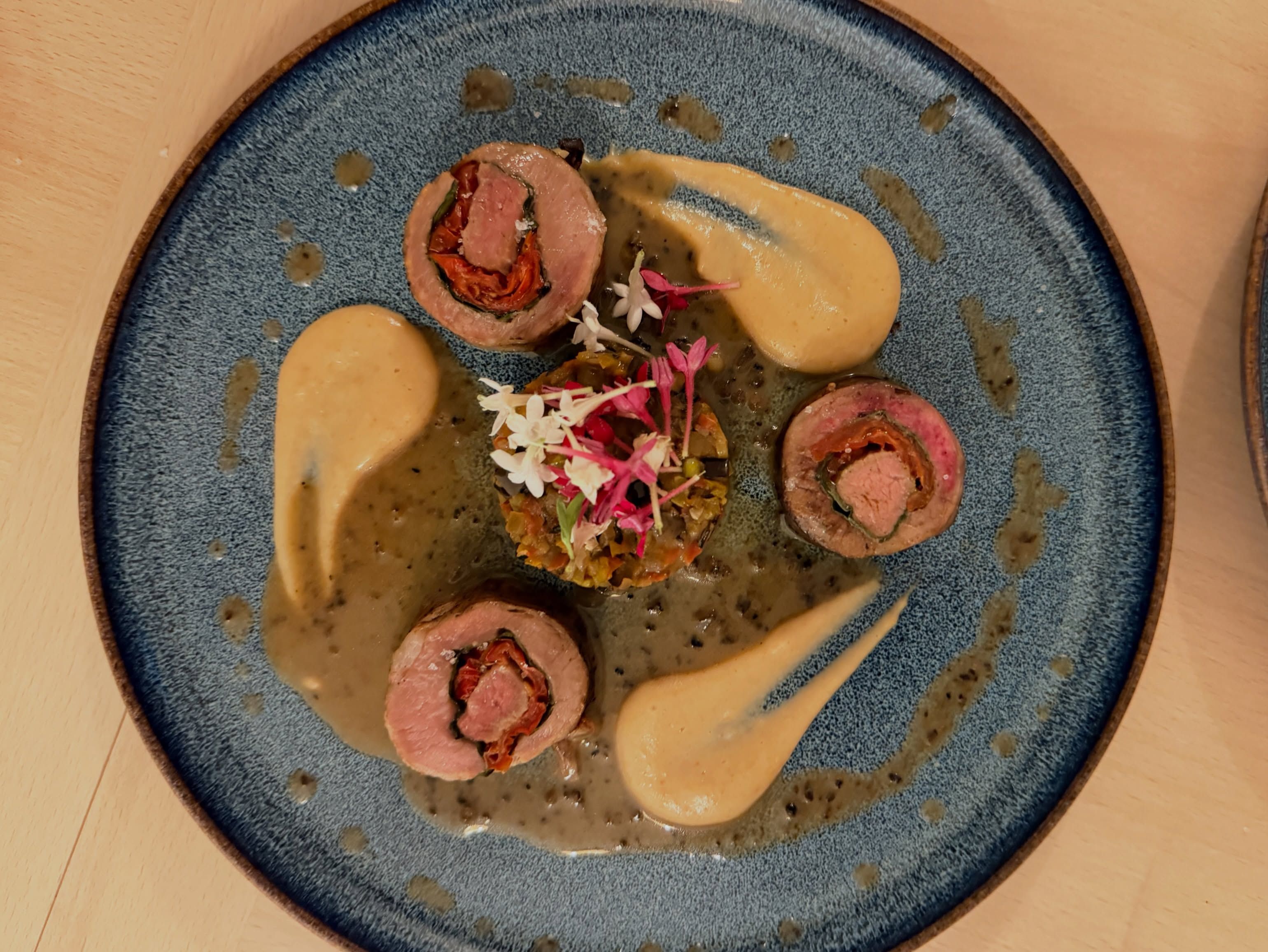 Provençal-stuffed saddle of lamb, ratatouille and garlic cream, plated on a blue plate.