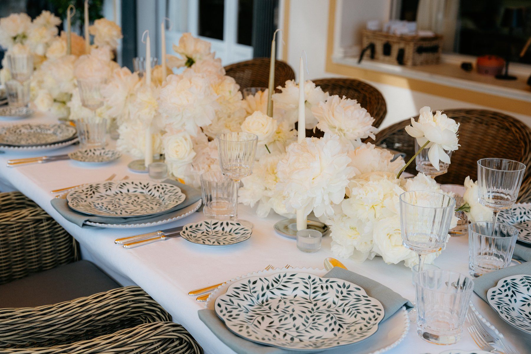 Long villa table dressed with white peonies, candelabras and patterned dinnerware.
