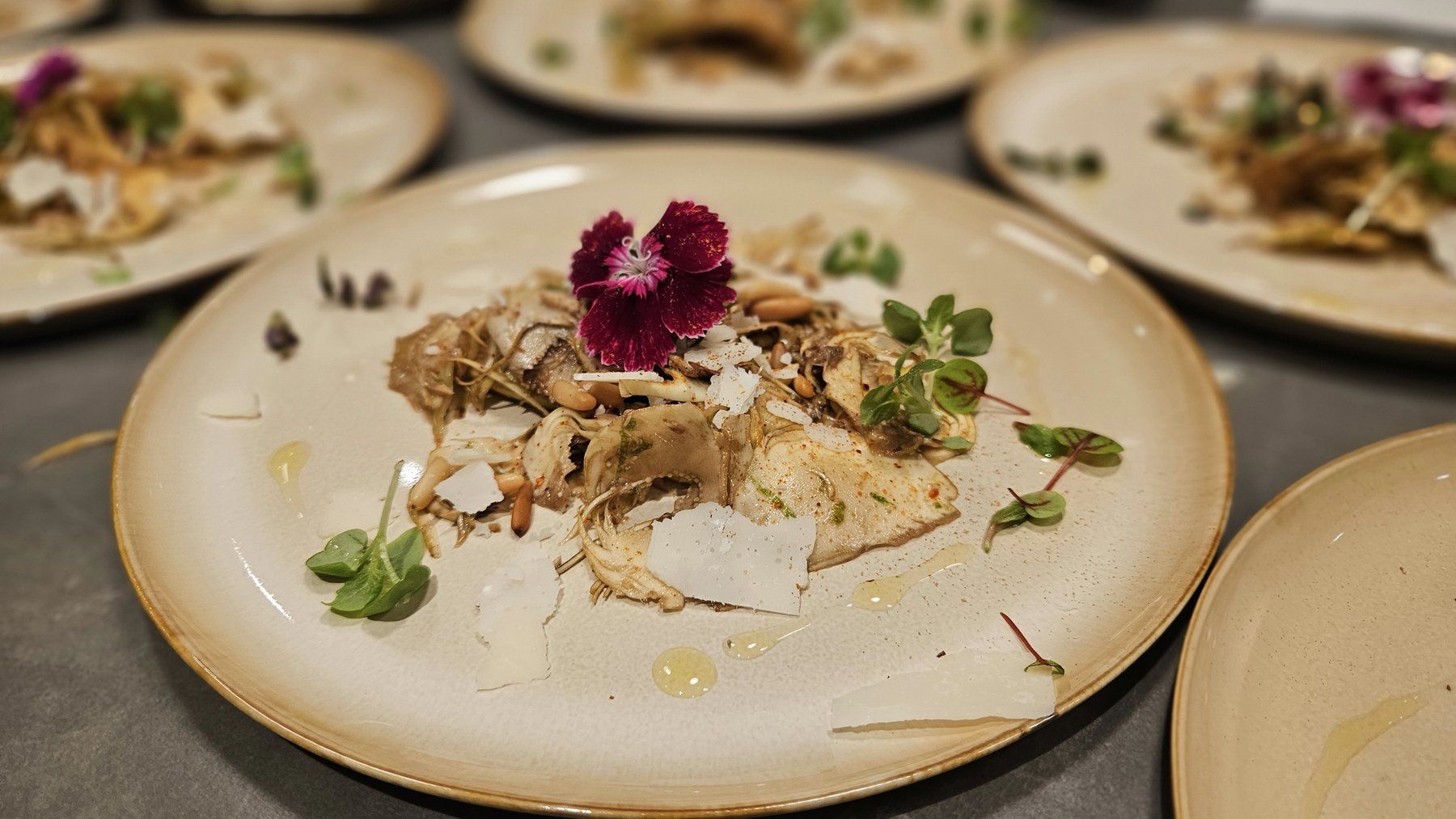 Fish course plated with shaved parmesan, pine nuts and edible flowers, served in multiples.